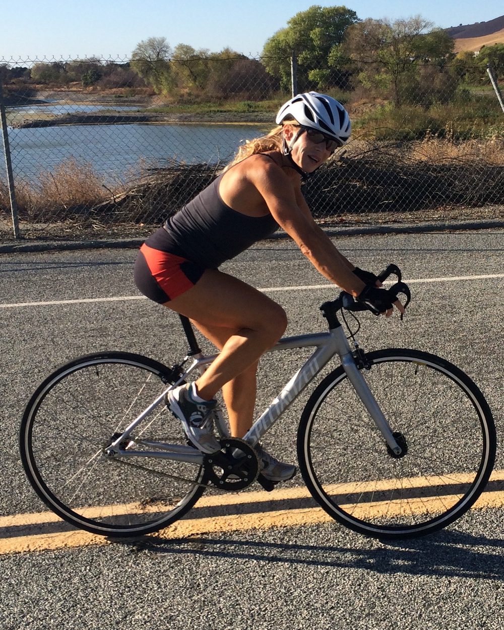 Loree riding a road bike along a country road beside a reservoir