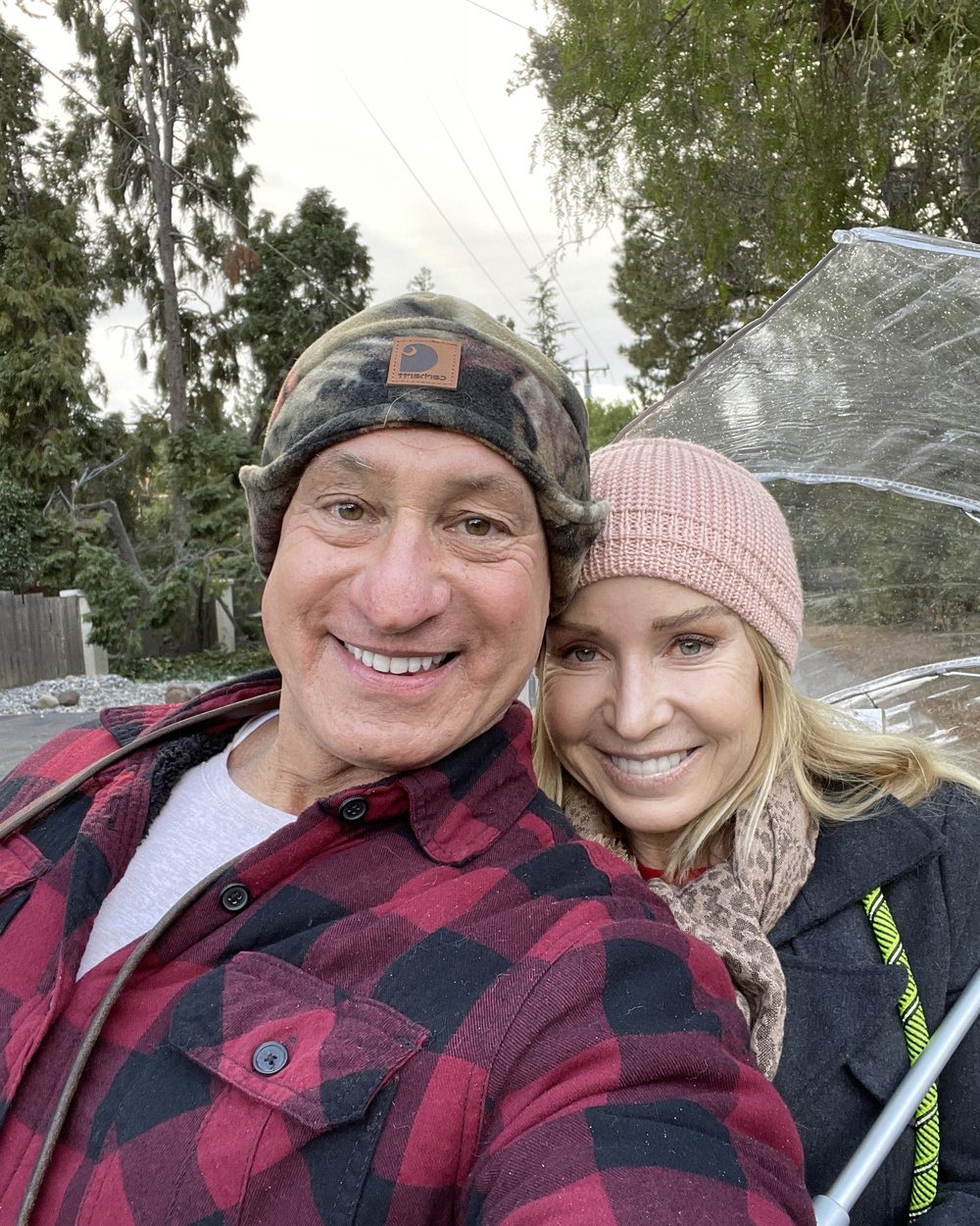 Ben in a plaid shirt and Loree in a pink beanie, outdoors under trees
